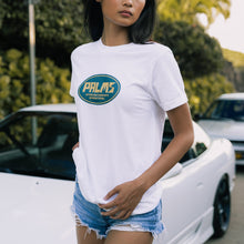 Load image into Gallery viewer, Person wearing a white t-shirt with a logo, standing in front of vintage cars.