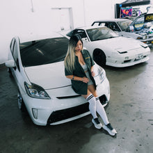 Load image into Gallery viewer, Woman leaning against a white car in an indoor setting with other cars in the background
