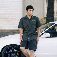 Load image into Gallery viewer, Man in a green shirt standing next to a white car with a palm tree in the background